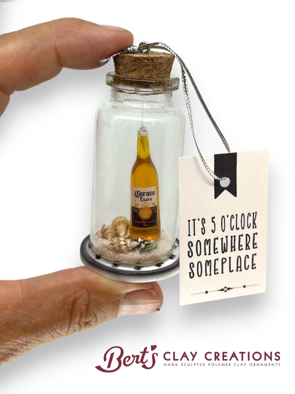 Miniature bottle with a Corona beer bottle inside, held by a hand, with a tag reading 'It's 5 o'clock somewhere someplace' by Berts Clay Creations.