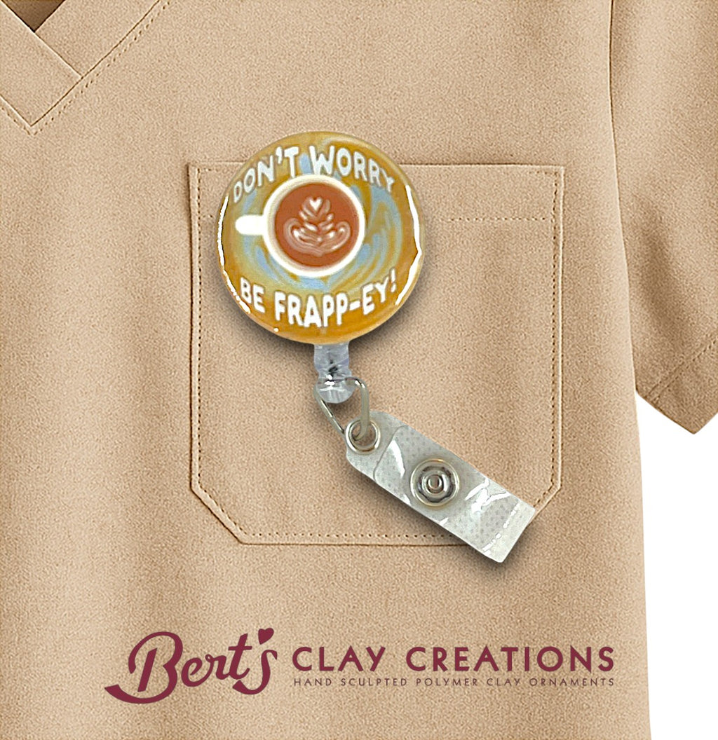 Badge holder with 'Don't Worry, Be Frapp-Ey!' design on a beige shirt, featuring Bert's Clay Creations branding.