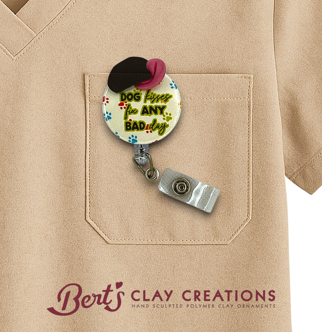 Retractable badge holder with 'Dog kisses fix Any Bad Day' text on a beige shirt, featuring Bert's Clay Creations branding.