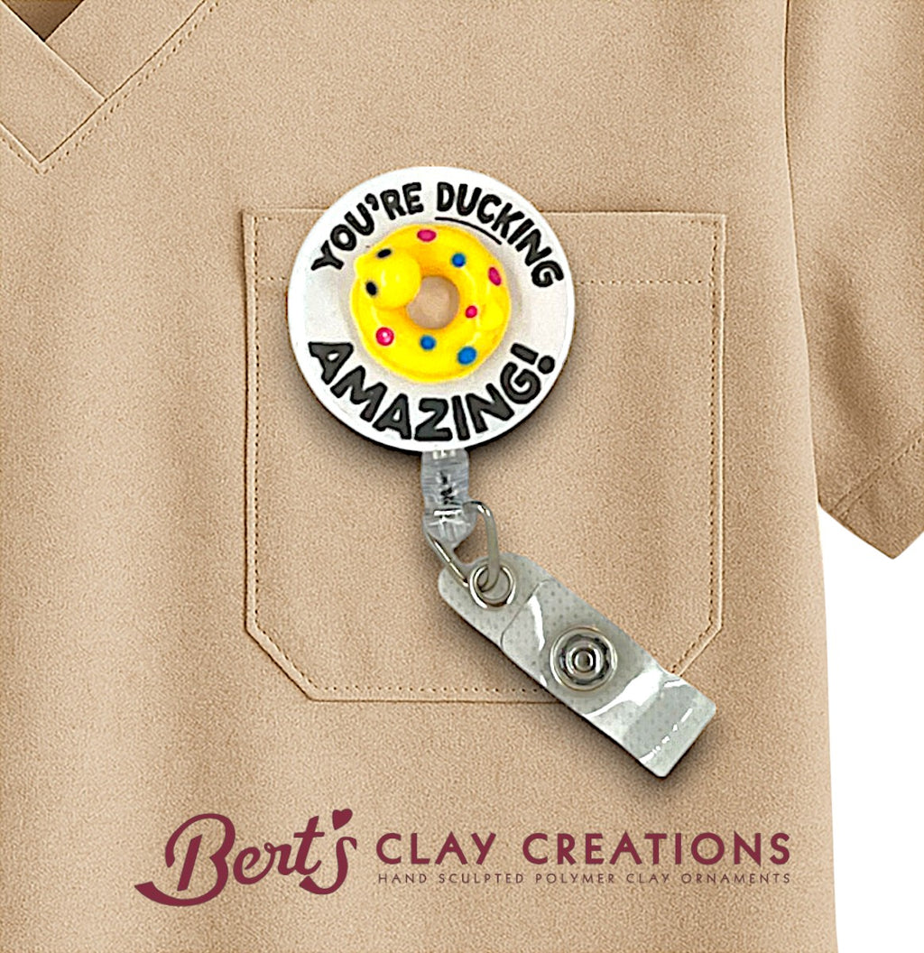 Badge holder with 'You're Ducking Amazing!' text and colorful design on a beige shirt pocket, featuring Bert's Clay Creations branding.