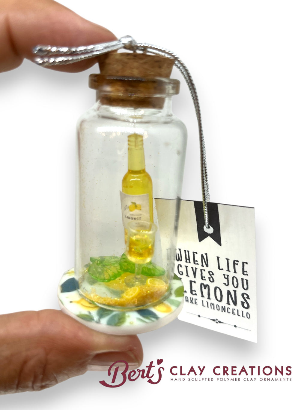 Decorative bottle with lemon and limoncello inside, held by a hand with 'Bert's Clay Creations' branding.