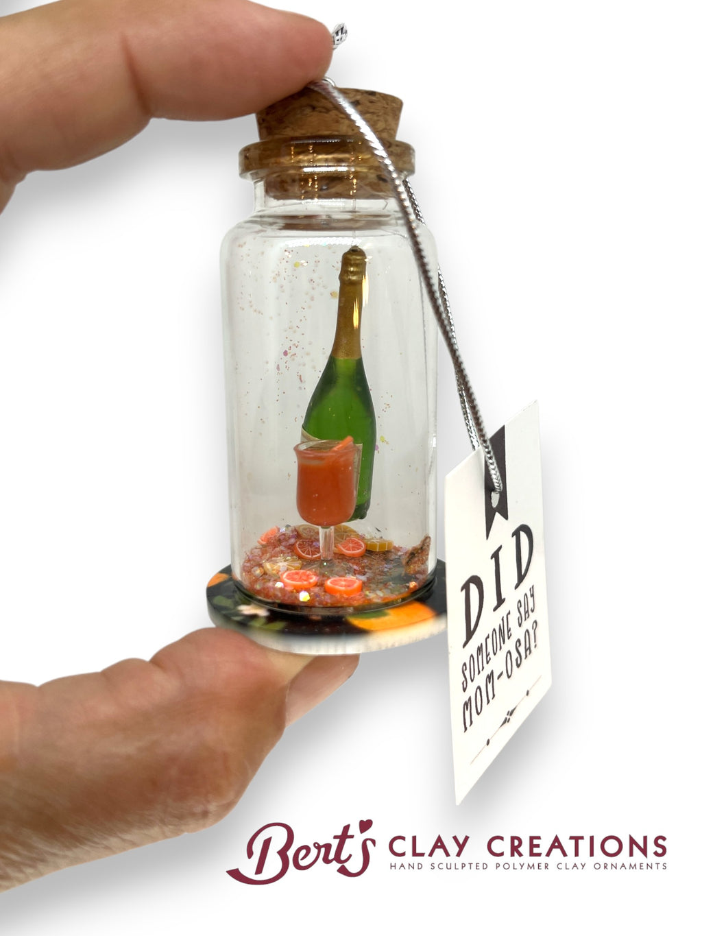 Miniature bottle with a scene inside, held by a hand, with 'Bert's Clay Creations' branding.