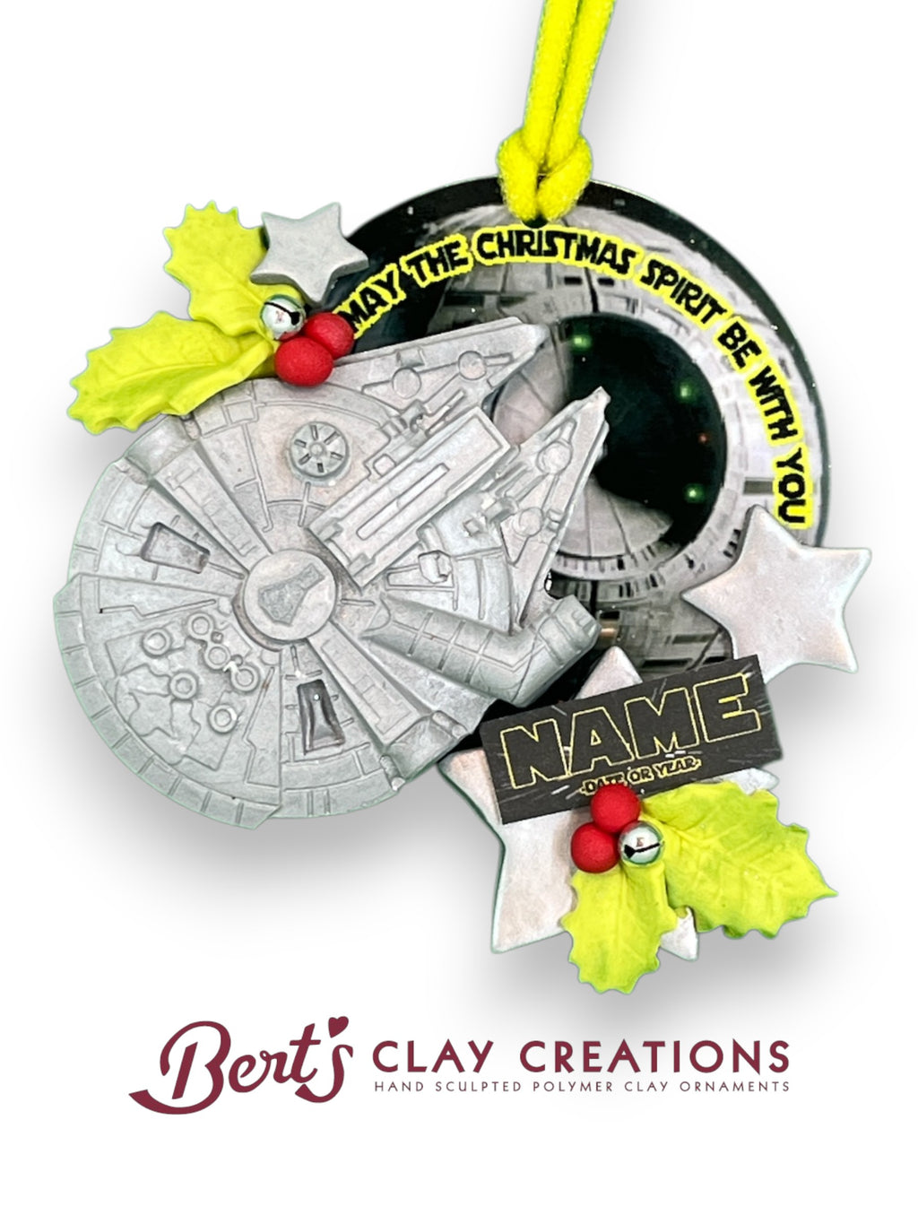 “Hand-sculpted polymer clay ornament featuring spaceship, holly accents, glittery stars, and ‘May the Christmas Spirit Be With You’ text with customizable nameplate – by Bert’s Clay Creations.”