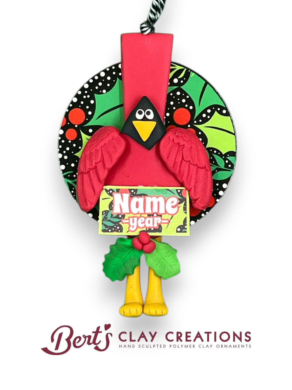 “Hand-sculpted polymer clay cardinal ornament with festive patterned background, holly accents, and customizable name/year plaque – by Bert’s Clay Creations.”
