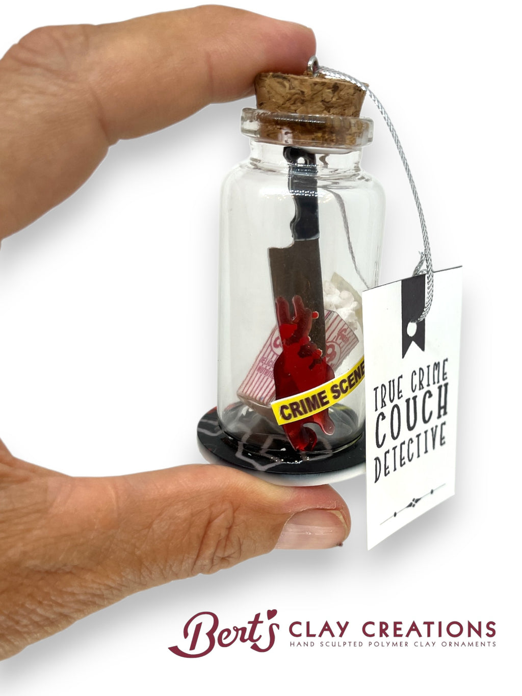 Glass bottle with cork lid containing a small sculpture labeled 'True Crime Couch Detective' by Berts Clay Creations.