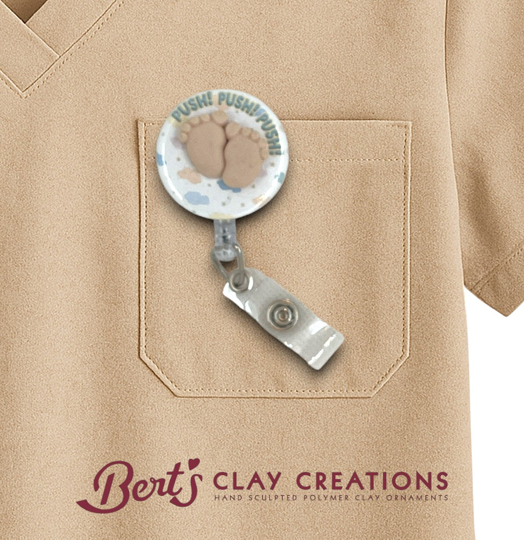 Retractable badge holder with baby feet design on a beige shirt, featuring 'Bert's Clay Creations' branding.