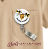 Retractable badge holder with bee design and 'Bee-lieve in Yourself' text, attached to a beige shirt pocket with 'Bert's Clay Creations' branding.