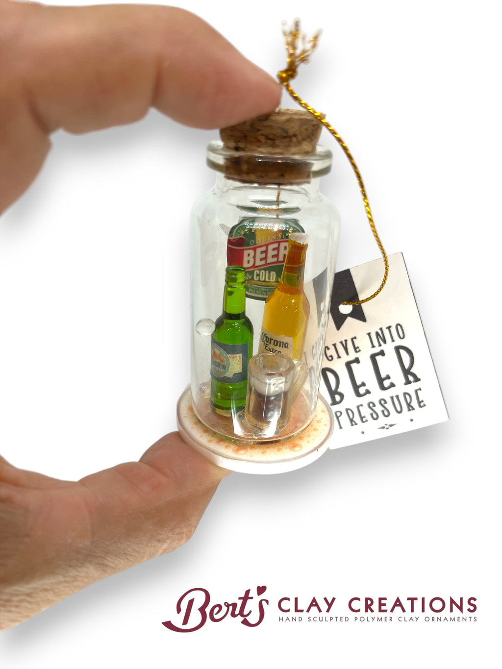 Miniature bottle scene in a glass jar held by a hand, with a 'Give into Beer Pressure' tag, branded 'Bert's Clay Creations'.