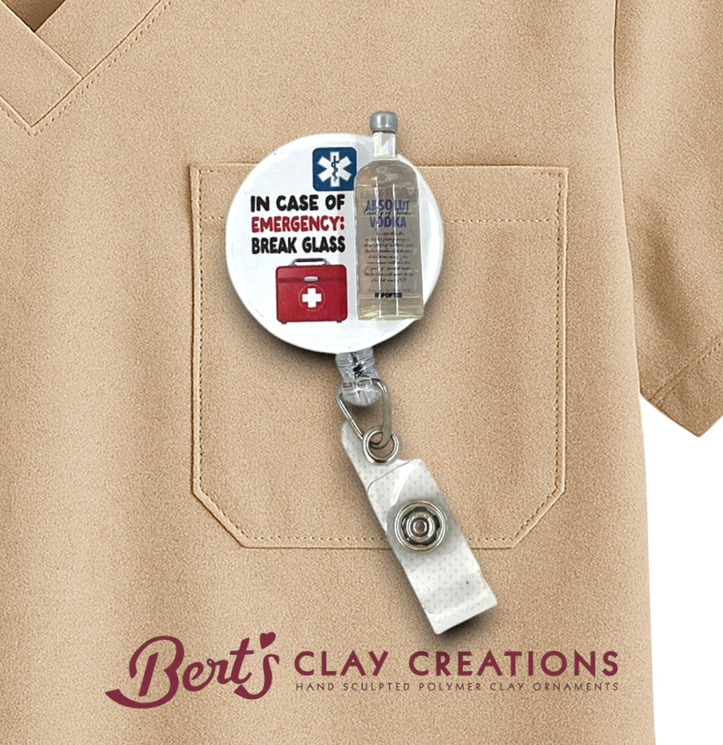 Retractable badge holder with humorous emergency label attached to a beige shirt, featuring 'Bert's Clay Creations' branding.