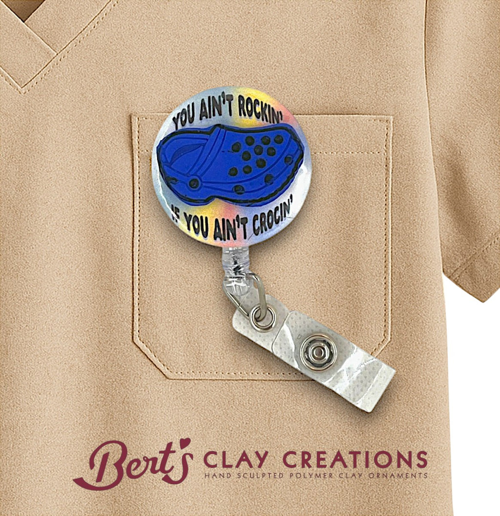Retractable badge holder with blue shoe design and text on a beige shirt, featuring 'Bert's Clay Creations' branding.