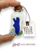 Small glass bottle with a blue clay croc inside, held by a hand, with a tag and 'Bert's Clay Creations' branding.