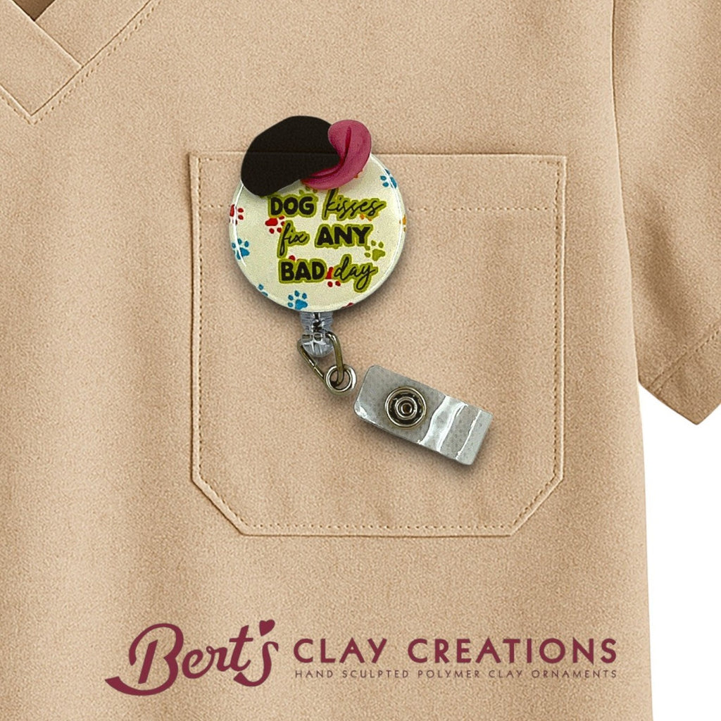 Retractable badge holder with 'Dog kisses fix Any Bad Day' text on a beige shirt, featuring Bert's Clay Creations branding.