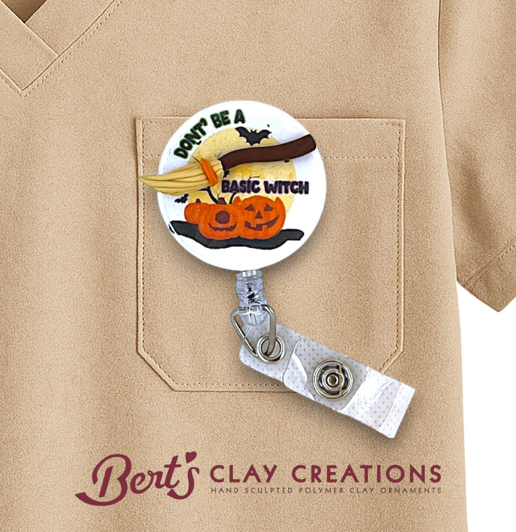 Halloween-themed badge holder with pumpkins and broomstick on a beige shirt, featuring 'Bert's Clay Creations' logo.