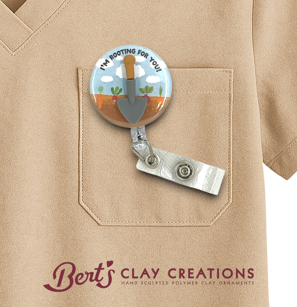 Retractable badge holder with garden-themed design on a beige shirt, featuring 'Bert's Clay Creations' branding.