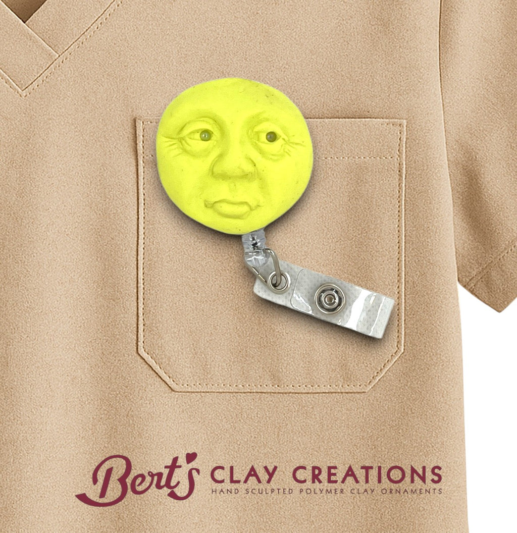 Yellow clay face attached to a badge holder on a beige shirt with 'Bert's Clay Creations' branding.