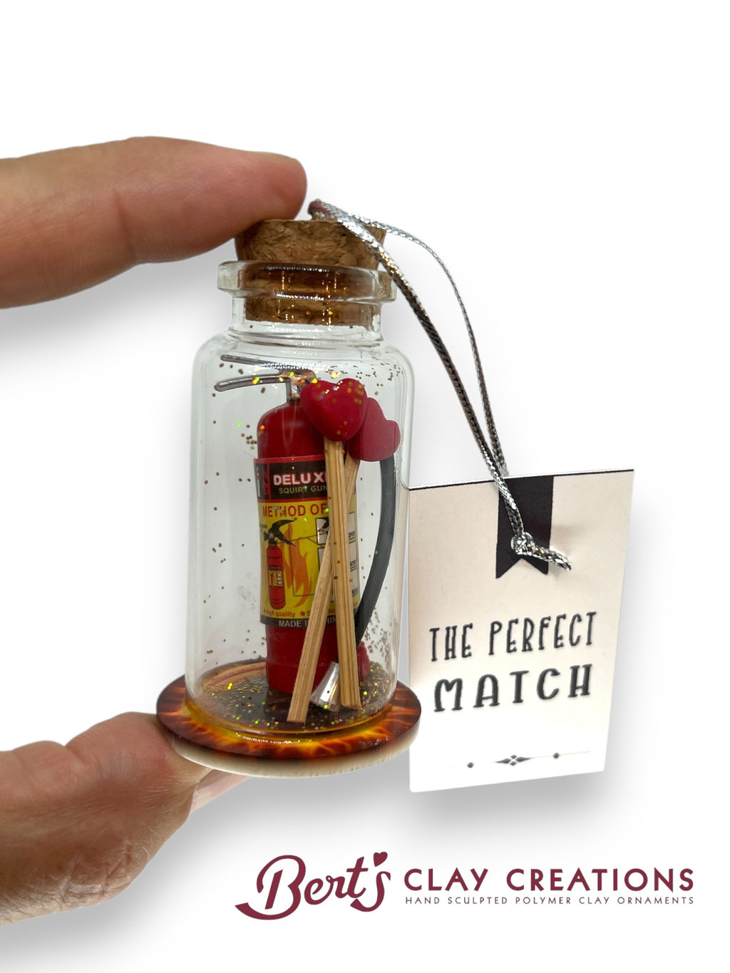 Miniature fire extinguisher and matches in a bottle with 'Bert's Clay Creations' branding.