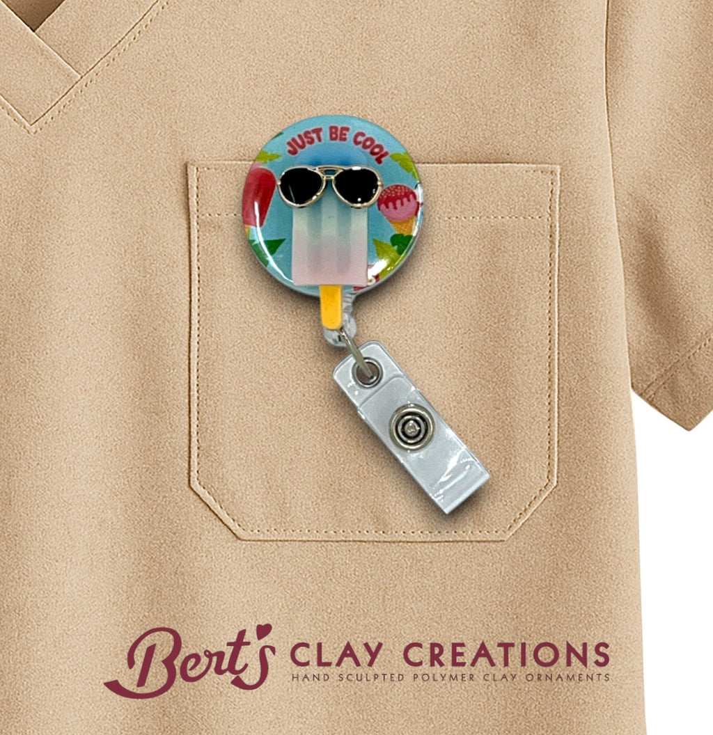 Colorful badge holder with sunglasses design attached to a beige shirt, featuring 'Bert's Clay Creations' branding.