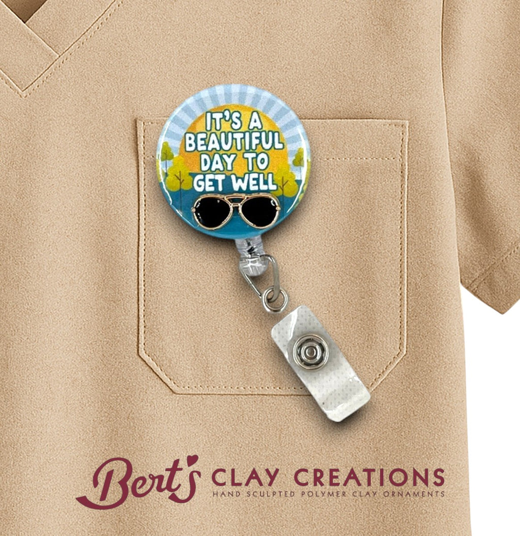 Retractable badge holder with 'It's a Beautiful Day to Get Well' design on a beige shirt, featuring Bert's Clay Creations logo.