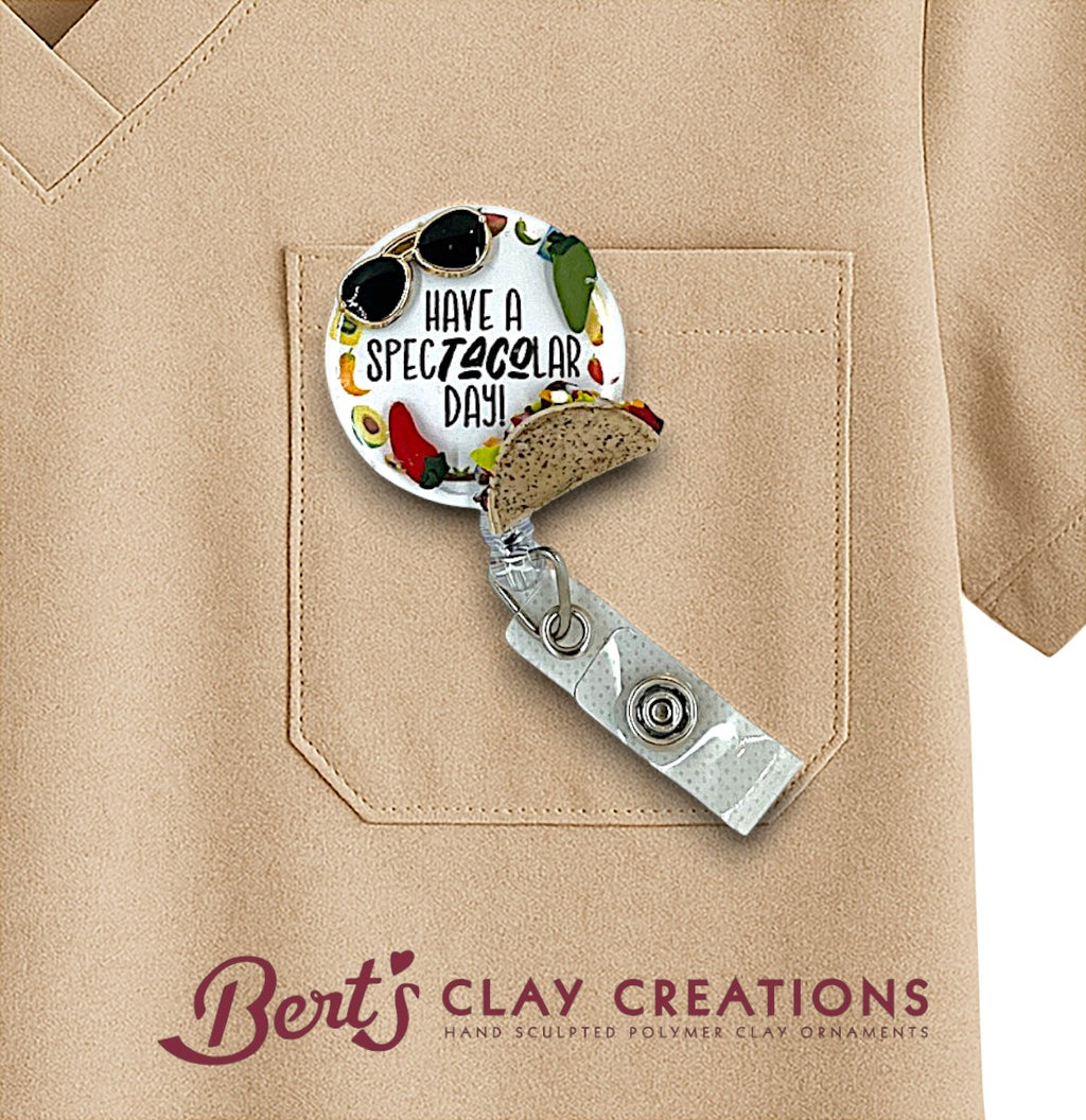 Badge holder with 'Have a Spectacular Day!' text and taco design, attached to a beige shirt pocket with 'Bert's Clay Creations' branding.