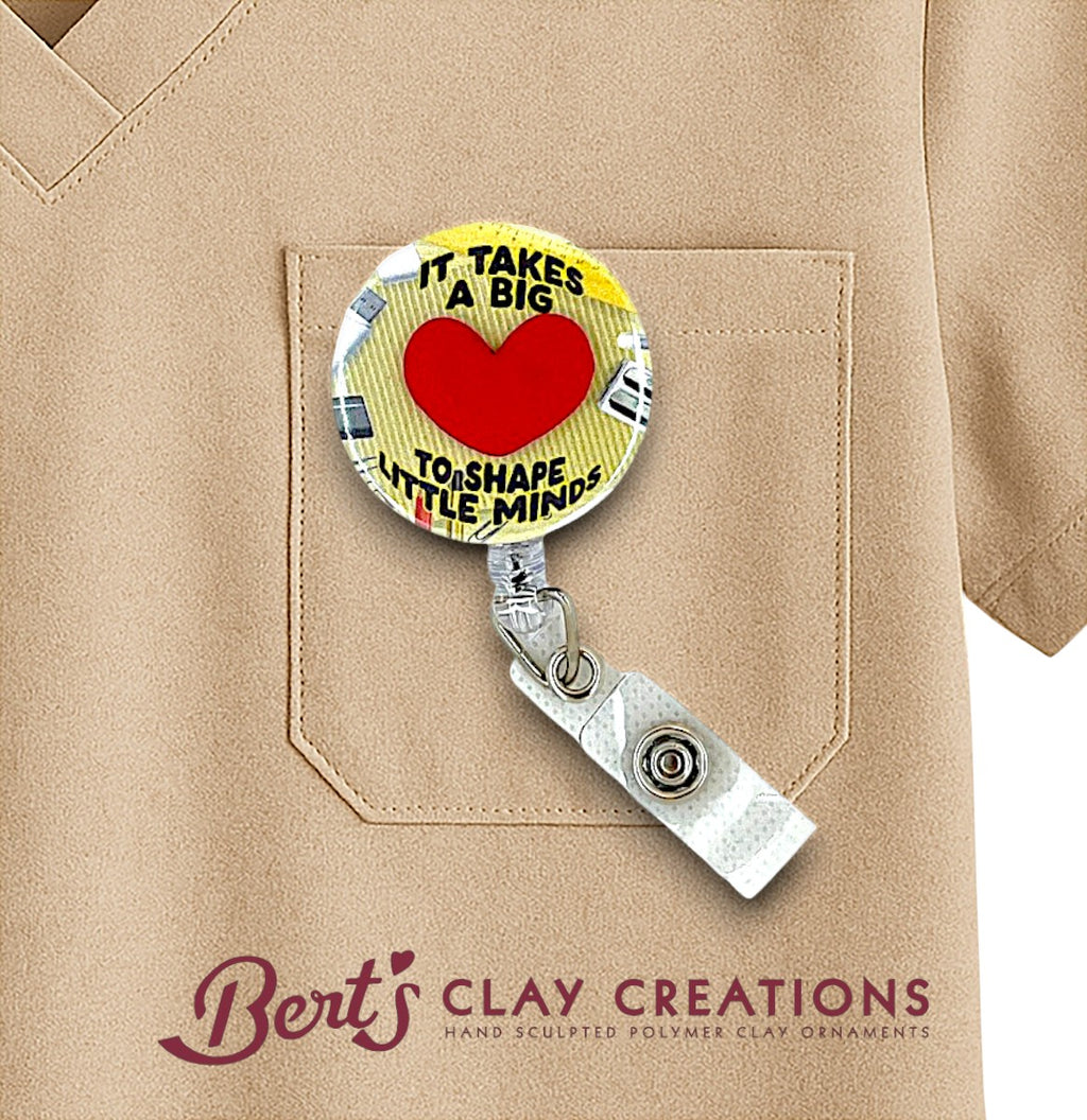 Retractable badge holder with a heart design and text on a beige shirt, featuring 'Bert's Clay Creations' branding.