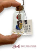 Hand holding a small glass jar with a cork lid containing teacher or education decorative items, with 'Bert's Clay Creations' branding.
