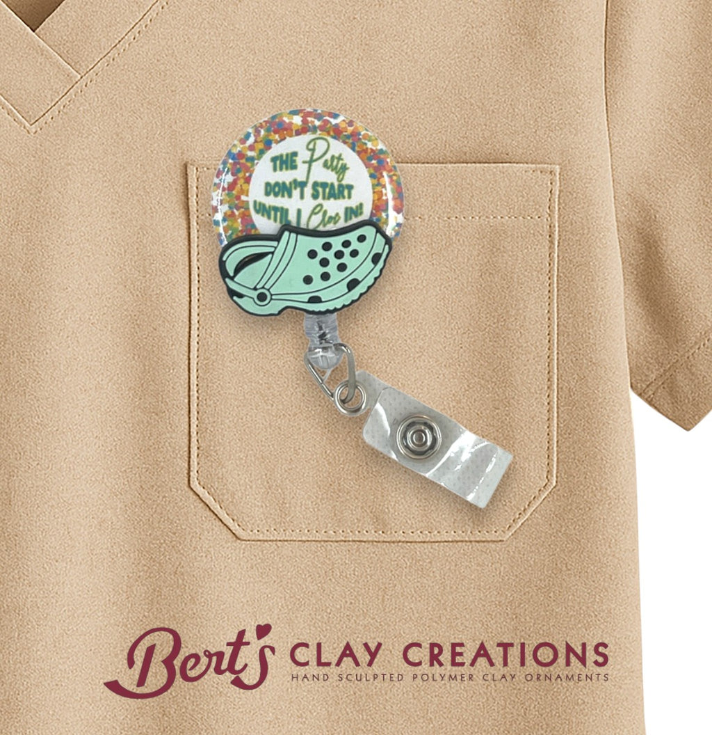 Retractable badge holder with colorful design attached to a beige shirt pocket, featuring 'Bert's Clay Creations' branding.
