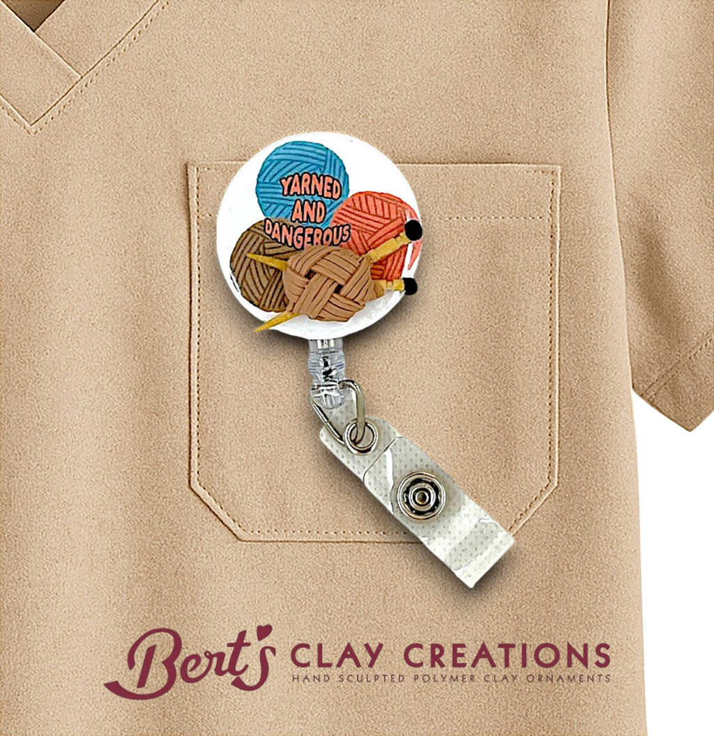 Retractable badge holder with yarn and clay design on a beige shirt, featuring 'Bert's Clay Creations' branding.
