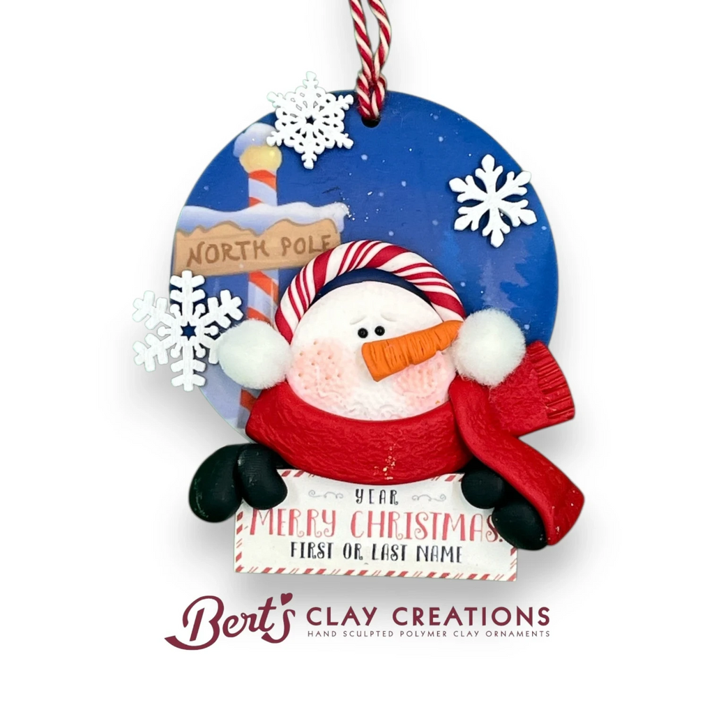 Bert's Clay Creations handcrafted snowman ornament with red scarf, North Pole sign, and personalized name space.