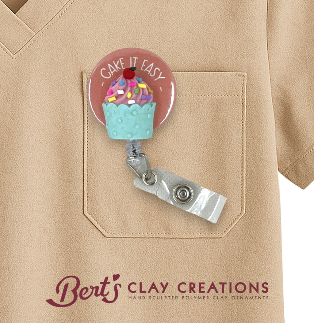 Badge holder with cupcake design and 'Cake It Easy' text on a beige shirt, branded with 'Bert's Clay Creations'.