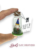 Hand holding a jar with a gnome decoration and 'Let's Far-tee' tag, with 'Bert's Clay Creations' branding.