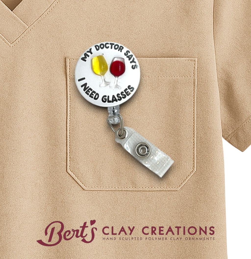 Retractable badge holder with 'My doctor says I need glasses' design on a beige shirt with 'Bert's Clay Creations' branding.
