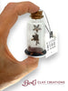 Hand holding a small glass bottle with star-shaped object and cork lid, branded 'Bert's Clay Creations'.